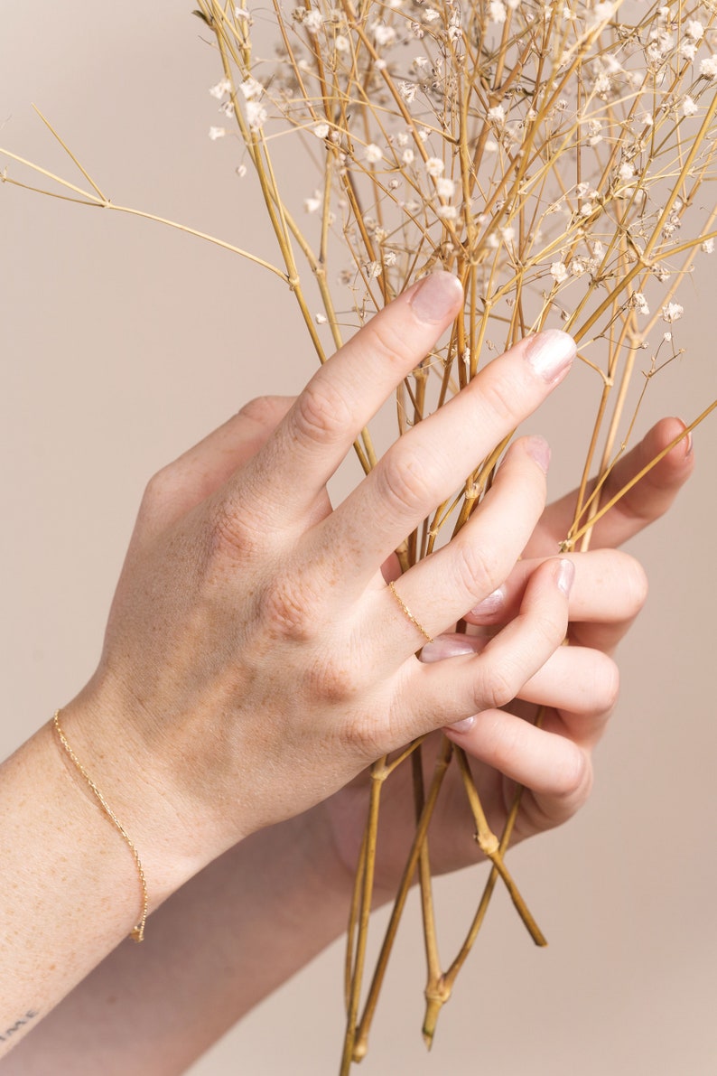 K&ouml;nnte beinhalten: Die H&auml;nde einer Person halten einen Strau&szlig; getrockneter Baby's Breath. Die Person tr&auml;gt ein zartes goldenes Kettenarmband und einen d&uuml;nnen goldenen Ring an ihrem Finger.