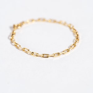K&ouml;nnte beinhalten: Ein goldenes Kettenarmband mit einem zarten, verlinkten Design. Die Kette besteht aus kleinen, rechteckigen Gliedern.