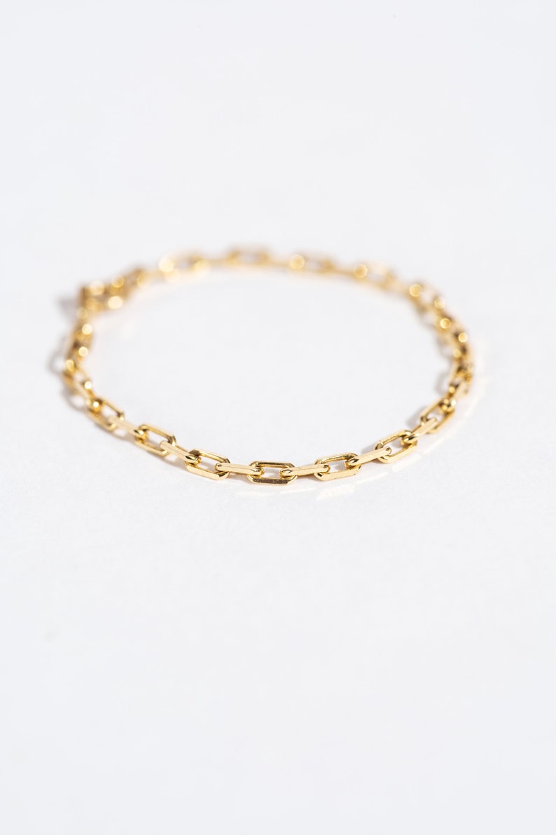 K&ouml;nnte beinhalten: Ein goldenes Kettenarmband mit einem zarten, verlinkten Design. Die Kette besteht aus kleinen, rechteckigen Gliedern.