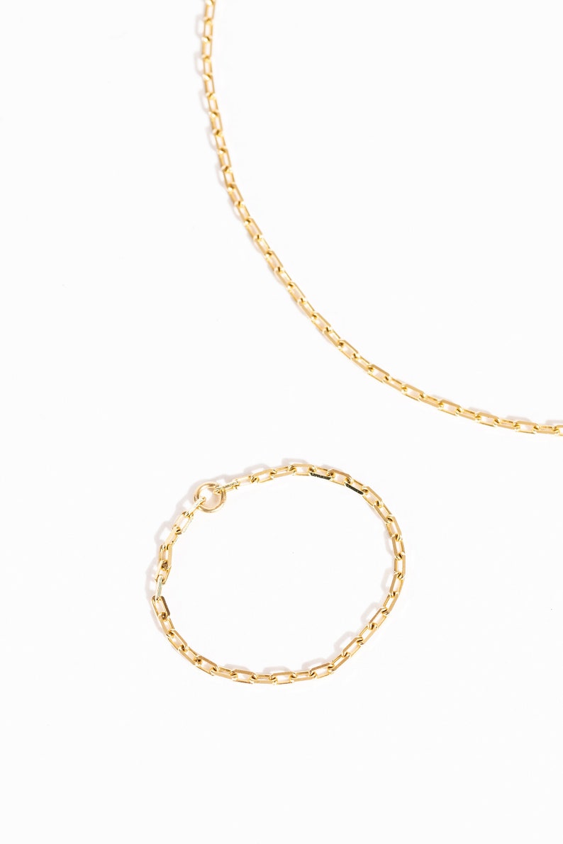 K&ouml;nnte beinhalten: Ein Set aus zwei goldenen Ketten, eine lange und eine kurze, mit einem zarten, rechteckigen Kettenmuster.