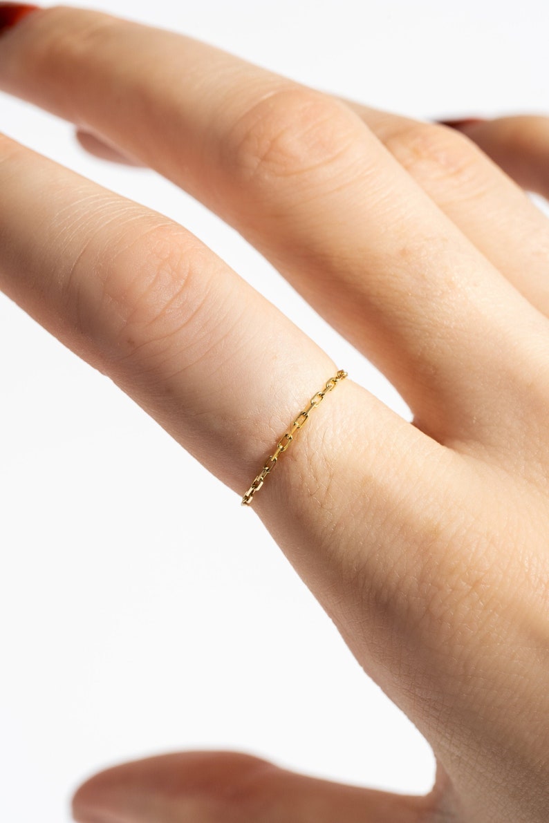 K&ouml;nnte beinhalten: Ein zarter goldener Kettenring, der an einem Finger getragen wird.