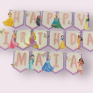 May include: A pink and white banner with the words "Happy Birthday Maia" decorated with Disney Princess characters. Each letter is adorned with a different princess, including Ariel, Belle, Cinderella, Snow White, and more.