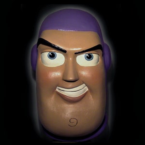 Puede incluir: Una máscara de plástico morada y marrón de un personaje de dibujos animados con una gran sonrisa y el número 9 en la barbilla.