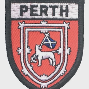 Op de afbeelding: Geborduurde patch met het woord "PERTH" in zwarte letters op een witte achtergrond. De patch heeft een rood schildontwerp met een wit lam dat een vlag vasthoudt. De rand is zwart.