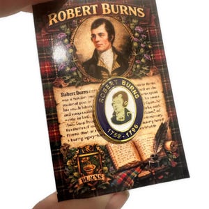 May include: A pin featuring a portrait of Robert Burns, with the text "ROBERT BURNS" at the top. The pin is on a card with a portrait of Robert Burns and text about his life. The pin has the text "ROBERT BURNS" and the years 1759-1796.