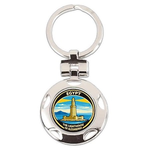 May include: Silver-colored keychain with a round charm featuring a colorful image of the Lighthouse of Alexandria, with the word "EGYPT" and "THE LIGHTHOUSE OF ALEXANDRIA" in black text. The keychain has a split ring for keys.