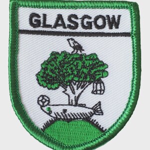May include: Embroidered patch with a green border and a white background. The patch features the word "GLASGOW" in black, a green tree, a bird, a fish, and a cage. The patch is a shield shape.