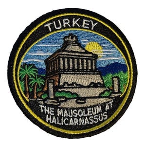 May include: Embroidered patch depicting the Mausoleum at Halicarnassus in Turkey. The patch has a black border with yellow trim, and the text "TURKEY" and "THE MAUSOLEUM AT HALICARNASSUS" are displayed. The image includes a blue sky, a yellow sun, palm trees, and mountains.