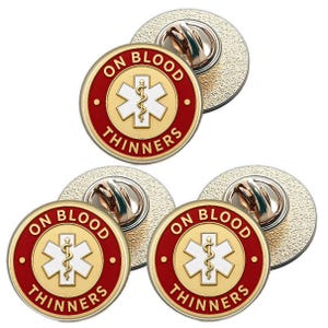 Può includere: Un set di sei spille rotonde con bordo rosso e centro dorato. Le spille presentano il testo "ON BLOOD THINNERS" attorno a un simbolo medico dorato. I retro delle spille sono argentati.