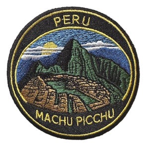 May include: Embroidered patch featuring a scenic view of Machu Picchu in Peru. The design includes a mountain range, the sun, and the text "PERU" and "MACHU PICCHU" in gold lettering on a black background with a gold border.