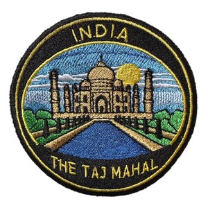 May include: Circular embroidered patch depicting the Taj Mahal in India. The patch has a black border with gold trim. The Taj Mahal is shown in beige, set against a blue sky with a yellow sun. The text "INDIA" and "THE TAJ MAHAL" are embroidered.