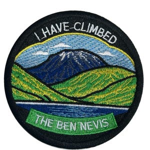 Puede incluir: Parche bordado circular con borde negro. El parche representa un paisaje montañoso con colinas verdes, agua azul y una cima. El texto incluye "I HAVE CLIMBED" y "THE BEN NEVIS" en letras blancas.