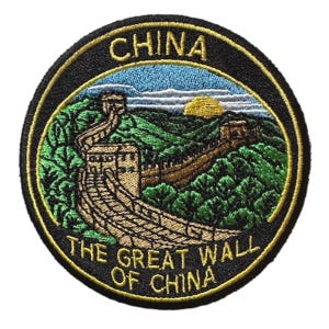 Pode incluir: Patch bordado circular com a Grande Muralha da China. O patch tem uma borda preta com a palavra "CHINA" na parte superior e "THE GREAT WALL OF CHINA" na parte inferior. A imagem mostra a muralha serpenteando por colinas verdes sob um céu azul.