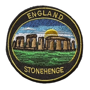 May include: Circular embroidered patch depicting Stonehenge, with the text "ENGLAND" and "STONEHENGE". The patch has a black border with a gold outline. The image shows a blue sky, green grass, and the monument in shades of brown.