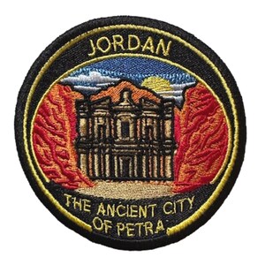Könnte beinhalten: Runder, gestickter Aufnäher mit dem Wort "JORDAN" oben. Der Aufnäher zeigt die antike Stadt Petra mit roten Felsformationen und blauem Himmel. Der Rand ist schwarz mit goldfarbenem Besatz und dem Text "THE ANCIENT CITY OF PETRA".