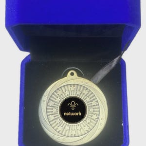 May include: A gold-colored medal with a star pattern and the word "network" in a black circle, presented in a blue velvet box. The medal has a loop for a ribbon.