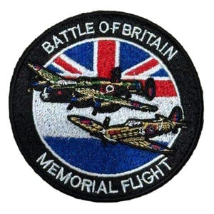 Op de afbeelding: Ronde geborduurde patch met twee gevechtsvliegtuigen tegen een Union Jack-achtergrond. De patch heeft de tekst "BATTLE O-BRITAIN MEMORIAL FLIGHT" in witte letters op een zwarte rand. De vliegtuigen zijn gedetailleerd met camouflagepatronen.