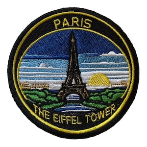 Könnte beinhalten: Gestickter Aufnäher mit dem Eiffelturm in Paris. Das Design umfasst einen blauen Himmel, eine gelbe Sonne und die Texte "PARIS" und "THE EIFFEL TOWER" in Gelb. Der Aufnäher hat einen schwarzen Rand mit gelben Nähten.