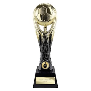 Könnte beinhalten: Eine gold-schwarze Fußballtrophäe. Die Trophäe zeigt einen Fußball, der von einer Figur hochgehalten wird. Der Sockel ist schwarz mit einer goldenen Platte mit der Aufschrift "YOUR ENGRAVING HERE". Ein kleines Emblem eines Trainers ist ebenfalls sichtbar.