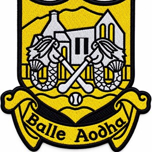 Peut inclure: Un écusson brodé jaune et noir représentant un blason avec deux sirènes tenant des crosses de hurling croisées devant un bâtiment. Une petite balle est placée sous les crosses et une bannière en bas affiche le texte Balle Aodha.