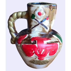 May include: A ceramic pitcher with a brown, white, red, and green painted design. The pitcher has a rope-like handle and a rounded body.
