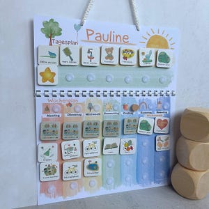 Könnte beinhalten: Ein farbenfroher Tages- und Wochenplan für Kinder mit dem Namen "Pauline" oben. Das Board verfügt über illustrierte Aktivitätskacheln und eine Aufhängeschnur. Der Hintergrund hat einen Aquarell-Effekt mit Pastellfarben.