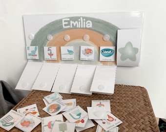 May include: A colorful rainbow-themed learning chart with the name "Emilia" at the top. The chart features various daily routine activities, such as brushing teeth, washing hands, and eating breakfast, represented by illustrated icons.  There are also several small cards with matching icons, likely used for a matching game or activity.