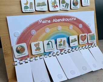 May include: A wooden board featuring a rainbow graphic labeled Meine Abendroutine with white square tiles depicting daily tasks like bathing, reading, and eating. The board includes white plastic tabs with velcro dots for tracking progress.