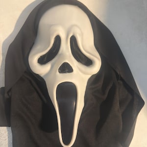May include: A white plastic ghost mask with elongated black eye sockets and a wide, open black mouth. The mask is attached to a black fabric hood that drapes around the sides and top, creating a full-face covering with a hollow, distorted expression.