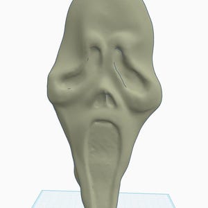 Op de afbeelding: Een lichtbeige masker met een vervormd, langwerpig gezicht. Het masker heeft een gapende mond en holle oogkassen, met een licht puntige kin. Het masker is een rekwisiet uit het horrorgenre.