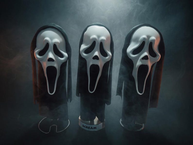 May include: Three white plastic masks with elongated black eye sockets and open mouths, each attached to a black fabric hood. The masks are mounted on individual stands, with the center base clearly displaying the word SCREAM in black letters.