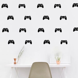 May include: Black controller decals arranged on a white wall. The controllers are evenly spaced and appear to be stickers or wall art. A white desk, chair, and decorative items are in the foreground.