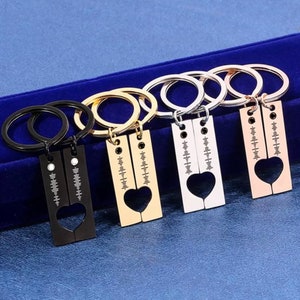 May include: Four keyrings with a heart-shaped cutout, in black, gold, silver, and rose gold finishes. Each keyring has a split design, forming a heart when joined. They also feature a music waveform design, with a circular keyring attachment.