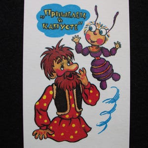 May include: A vintage postcard featuring two cartoon characters. One is a man in a red outfit with yellow polka dots and a black vest. The other is a purple insect-like creature. Text in a blue cloud bubble reads "Пришелец в капусте".