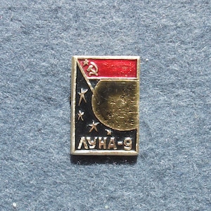 Puede incluir: Pin rectangular con una parte superior roja con un martillo y una hoz. Debajo, un campo negro con estrellas y un planeta dorado, con el texto cirílico "ЛУНА-9". Un recuerdo vintage de la exploración espacial.