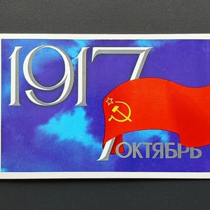 以下が含まれることがあります： 青い背景に「1917」の数字が銀色で描かれた長方形のステッカー。右側には、金色のハンマーと鎌と星が付いた赤い旗があります。「OKTYABR」という言葉が旗の下に銀色で書かれています。
