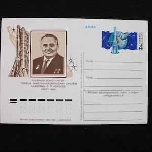 May include: Vintage postcard featuring a portrait of a man in a suit, with text in Russian. The postcard includes a stamp with a rocket and planet design. The overall theme is space exploration.