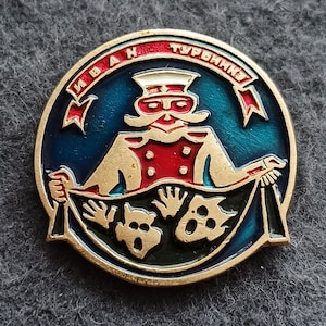 Puede incluir: Un pin redondo vintage con borde dorado y diseño de esmalte azul y rojo. El pin presenta una figura de dibujos animados con uniforme rojo y blanco sosteniendo una tela negra con tres figuras blancas con forma de calavera. El texto "ИВАН ТУРГЕНЕВ" está en rojo.