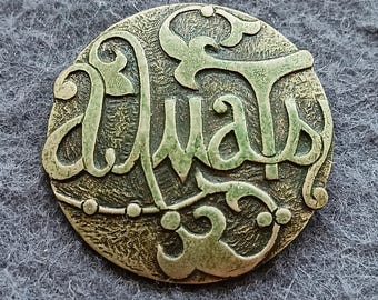 Può includere: Medaglione rotondo in metallo in stile antico con calligrafia araba. Il testo è di colore verde chiaro, su uno sfondo strutturato color bronzo. Il design include elementi decorativi.