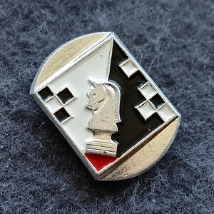 May include: A silver-toned chess knight pin with a geometric design. The pin features a white and black background with a chess knight in the center. The bottom of the pin has a red triangle.