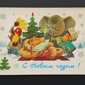 Puede incluir: Postal vintage con una ilustración caprichosa de una serpiente durmiente, un elefante, un mono y un loro. La escena incluye un árbol de Navidad y copos de nieve, con texto en ruso. El tema general es un saludo festivo.