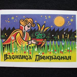 Puede incluir: Ilustración colorida que presenta una figura con un atuendo amarillo y rojo sosteniendo una rana en un cuenco. El fondo muestra un cielo nocturno con estrellas y una luna amarilla, con el texto "Василиса Прекрасная" en la parte inferior.