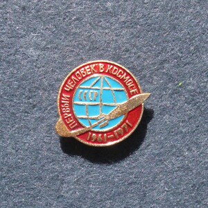 May include: A vintage round pin with a red and gold border. The pin features a blue globe with a rocket and the text "Первый человек в космосе" and "1961-1971". The pin is a commemorative item.