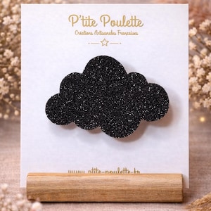 Peut inclure: Une barrette à cheveux noire en forme de nuage pailleté sur une carte blanche avec du texte doré. La carte est montée sur une base en bois. Le texte sur la carte indique "P'tite Poulette, Créations Artisanales Françaises".