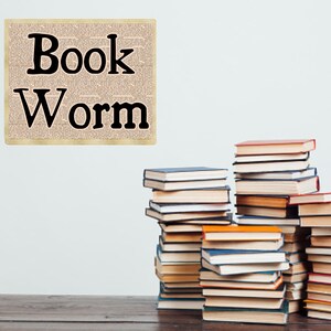 May include: A stack of books on a wooden table with a sign that says "Book Worm" on a white wall behind the books.