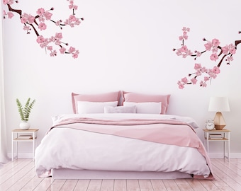 May include: A white bedroom with a pink bedspread and two pink pillows. The walls are decorated with pink cherry blossom decals.
