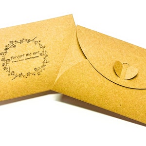 May include: Two brown paper envelopes. One envelope has a floral wreath design with the text "Forget me not" and "Forever loved, Never forgotten". The other envelope has a heart-shaped closure.