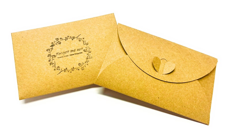 May include: Two brown paper envelopes. One envelope has a floral wreath design with the text "Forget me not" and "Forever loved, Never forgotten". The other envelope has a heart-shaped closure.