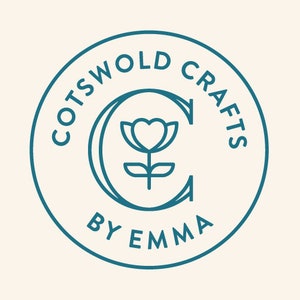 May include: Circular teal logo with the words "COTSWOLD CRAFTS" around the top and "BY EMMA" at the bottom. A teal "C" with a heart-shaped flower design is in the center. The background is a light beige color.
