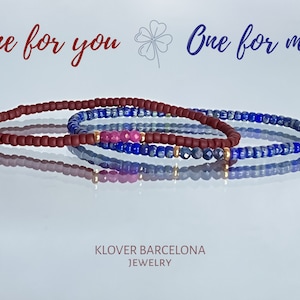 Puede incluir: Dos pulseras a juego, una con cuentas marrones y la otra con cuentas azules y detalles dorados. Las pulseras están apiladas una encima de la otra y tienen un reflejo en una superficie blanca. El texto "One for you" y "One for me" está por encima de las pulseras.